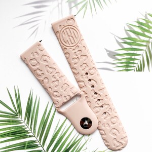 May include: A pair of pink silicone watch bands with a leopard print design. One band has a monogrammed circle in the center.