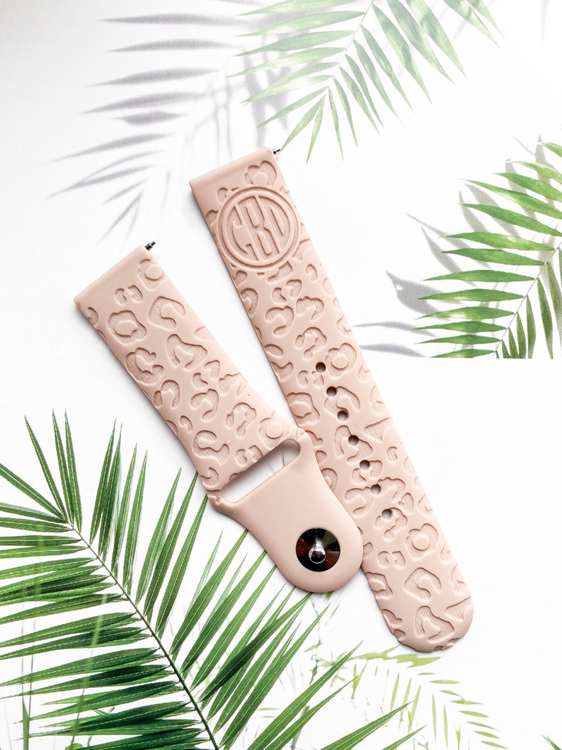 May include: A pair of pink silicone watch bands with a leopard print design. One band has a monogrammed circle in the center.
