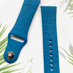 Op de afbeelding: Twee blauwe siliconen horlogebandjes met een Zelda-thema. E&eacute;n bandje heeft een zwaard en het andere heeft een Triforce en andere Zelda-symbolen.