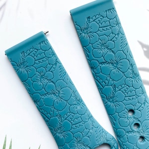 May include: Two teal blue silicone watch bands with a floral pattern. The bands have a textured surface and are designed to fit a wrist.