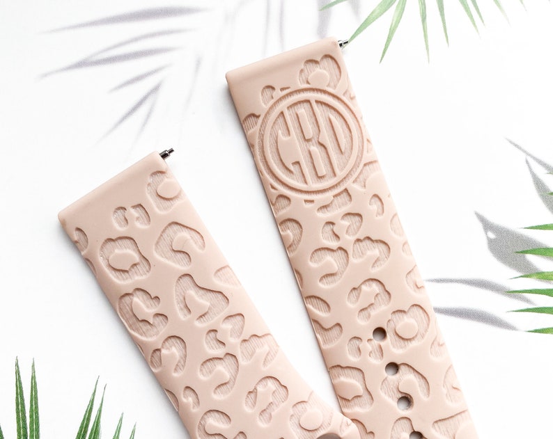 May include: Two blush pink silicone watch bands with a leopard print design. One band has a monogrammed circle with the letters "CBO" in the center.