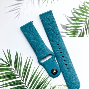 May include: Two teal blue silicone watch bands with a floral embossed pattern. The bands are designed for smartwatches.