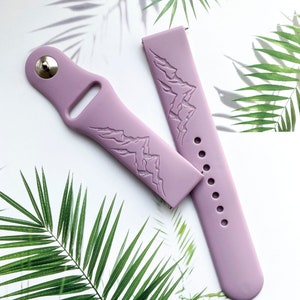 K&ouml;nnte beinhalten: Zwei lavendelfarbene Silikon-Uhrenarmb&auml;nder mit einem Bergketten-Design. Die Armb&auml;nder sind auf einem wei&szlig;en Hintergrund mit gr&uuml;nen Palmbl&auml;ttern abgebildet.