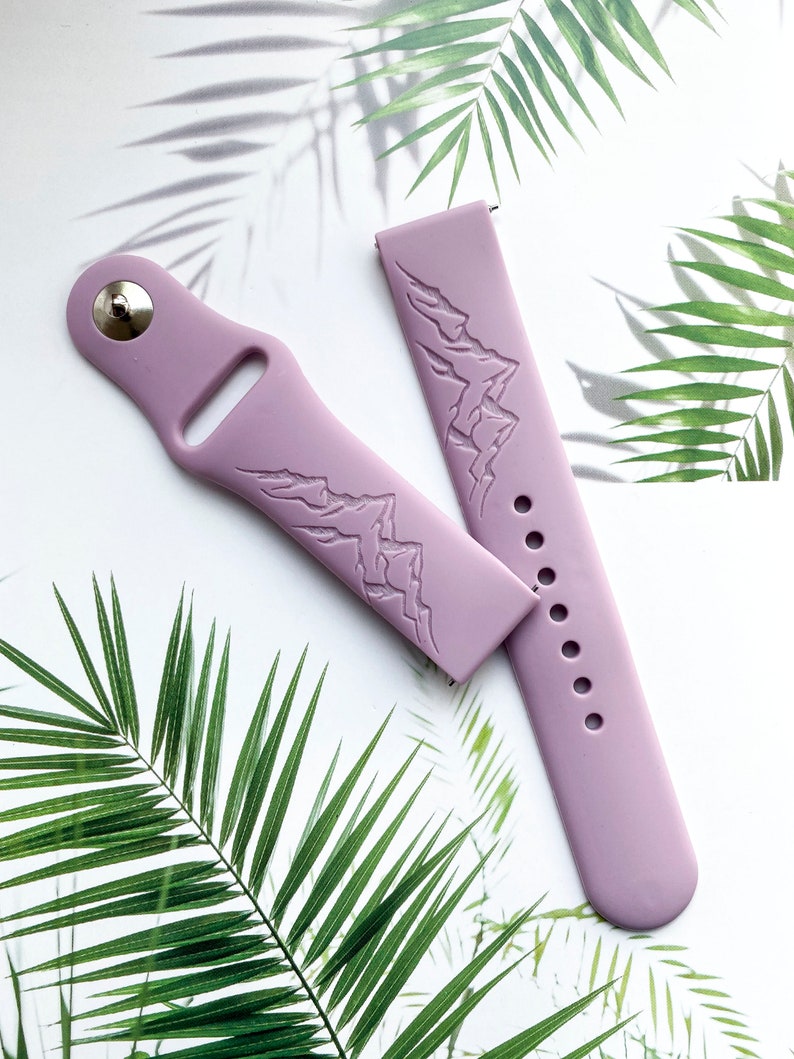 K&ouml;nnte beinhalten: Zwei lavendelfarbene Silikon-Uhrenarmb&auml;nder mit einem Bergketten-Design. Die Armb&auml;nder sind auf einem wei&szlig;en Hintergrund mit gr&uuml;nen Palmbl&auml;ttern abgebildet.