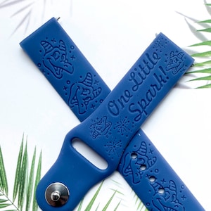 May include: A blue silicone watch band with a white inscription that reads "One little spark!" and a whimsical design of a witch's hat and stars.