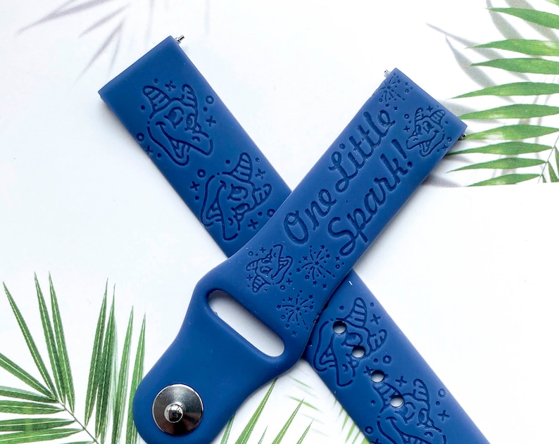 May include: A blue silicone watch band with a white inscription that reads "One little spark!" and a whimsical design of a witch's hat and stars.