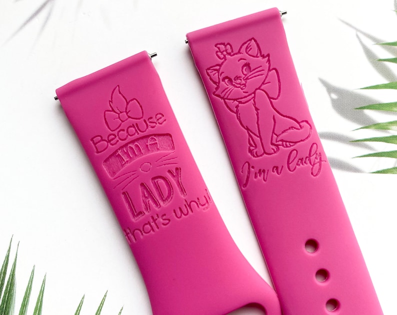 Op de afbeelding: Twee roze siliconen horlogebandjes met gegraveerde ontwerpen. E&eacute;n bandje heeft een cartoonkat met de tekst "Ik ben een dame". Het andere bandje heeft een strik en de tekst "Omdat ik een dame ben, dat is waarom!"