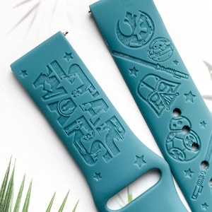 K&ouml;nnte beinhalten: Zwei tealblaue Silikon-Uhrenarmb&auml;nder mit gepr&auml;gten Star Wars-Charakteren und den Worten "Star Wars" auf einem Armband. Die Charaktere sind Darth Vader, Yoda, R2-D2 und ein Stormtrooper.