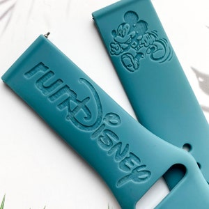 May include: Two teal blue silicone watch bands with embossed designs. One band features the words "Disney" and "Park" in a stylized font. The other band features a cartoon image of Mickey Mouse.