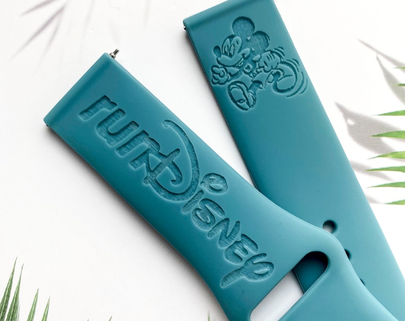 May include: Two teal blue silicone watch bands with embossed designs. One band features the words "Disney" and "Park" in a stylized font. The other band features a cartoon image of Mickey Mouse.