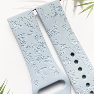 K&ouml;nnte beinhalten: Zwei hellblaue Silikon-Uhrenarmb&auml;nder mit einem wei&szlig;en Pr&auml;gemuster. Ein Armband zeigt den Text "Let's Get Lost" und "Mickey Mouse" mit einer Mickey Mouse-Silhouette. Das andere Armband zeigt den Text "Let's Get Lost" und "Disney World" mit einem Feuerwerksmuster.