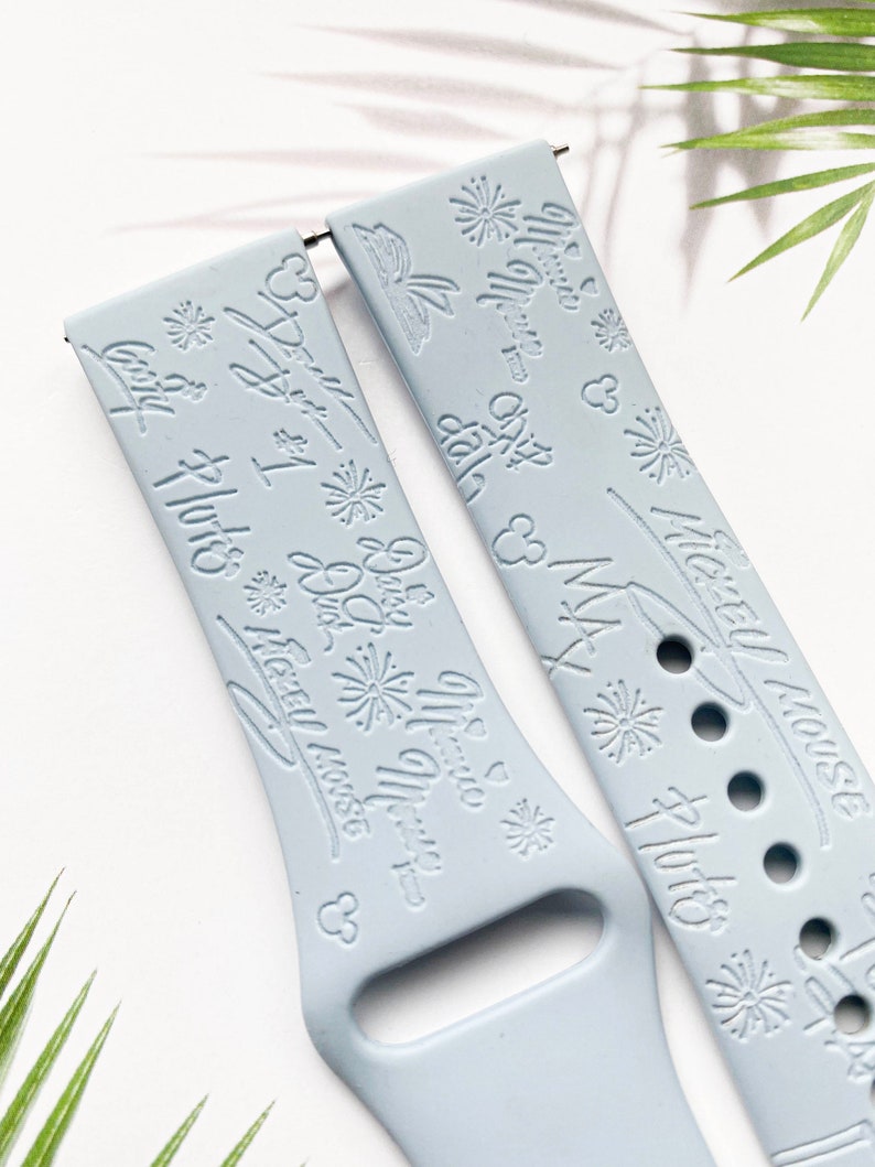 K&ouml;nnte beinhalten: Zwei hellblaue Silikon-Uhrenarmb&auml;nder mit einem wei&szlig;en Pr&auml;gemuster. Ein Armband zeigt den Text "Let's Get Lost" und "Mickey Mouse" mit einer Mickey Mouse-Silhouette. Das andere Armband zeigt den Text "Let's Get Lost" und "Disney World" mit einem Feuerwerksmuster.
