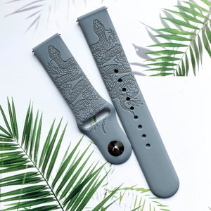 May include: Two gray silicone watch bands with a snake and floral design. The bands are embossed with a detailed pattern.