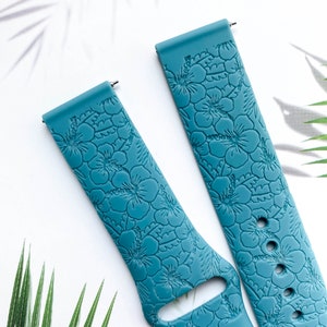 May include: Two teal blue silicone watch bands with a floral pattern. The bands have a textured surface and are designed for smartwatches.