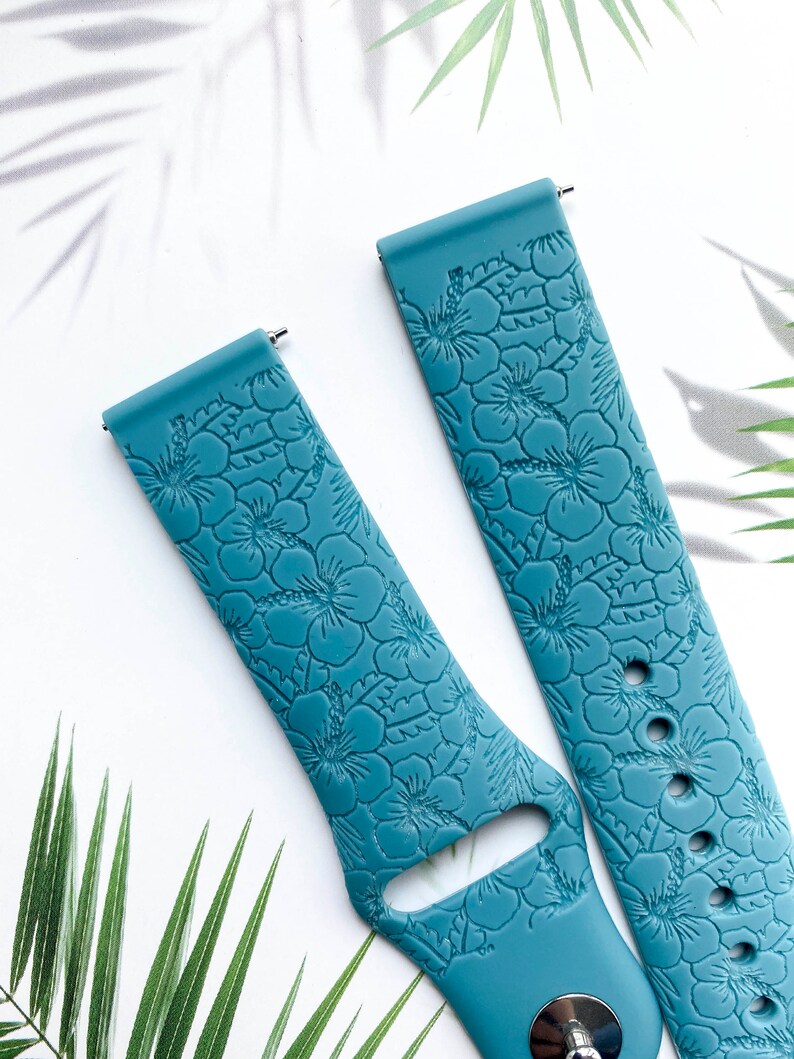 May include: Two teal blue silicone watch bands with a floral pattern. The bands have a textured surface and are designed for smartwatches.