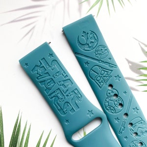 K&ouml;nnte beinhalten: Zwei tealblaue Silikon-Armb&auml;nder mit gepr&auml;gten Star Wars-Charakteren und dem Text "Star Wars".
