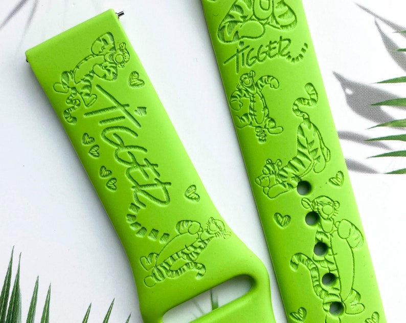 May include: Green watch band with a Tigger design. The band features a repeating pattern of Tigger's face and the word "Tigger" in a handwritten font.