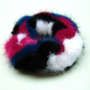 Könnte beinhalten: Ein flauschiger Haargummi in einem bunten Patchwork-Design. Der Haargummi ist aus schwarzem, weißem, rosa und blauem Fell.