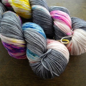 May include: Close-up of colourful yarn skeins. The yarn is a mix of grey, pink, yellow, and blue. The yarn is tightly wound and appears soft. Ideal for knitting or crocheting projects.