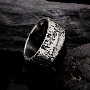 May include: A silver ring with a textured, hammered finish. The ring is wide and has a rough, organic look.