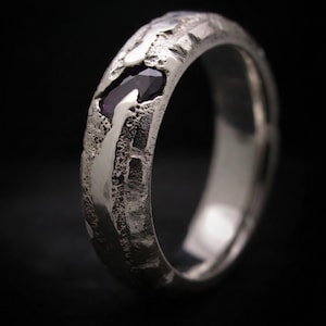 Peut inclure: Une bague en argent avec un anneau texturé et une pierre précieuse violet foncé. La bague a un design unique et robuste avec un intérieur poli. La pierre est sertie dans l'anneau.