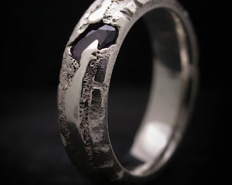 Può includere: Un anello d'argento con una fascia strutturata e una pietra preziosa viola scuro. L'anello ha un design unico e robusto con un interno lucido. La gemma è incastonata nella fascia.