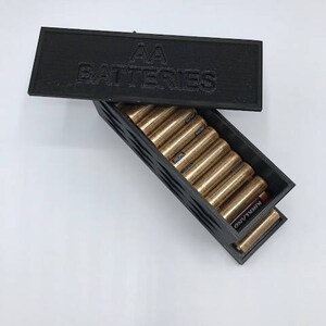 Puede incluir: Caja de almacenamiento de pl&aacute;stico negro con una tapa que dice "AA Batteries". La caja est&aacute; abierta y llena de bater&iacute;as AA.