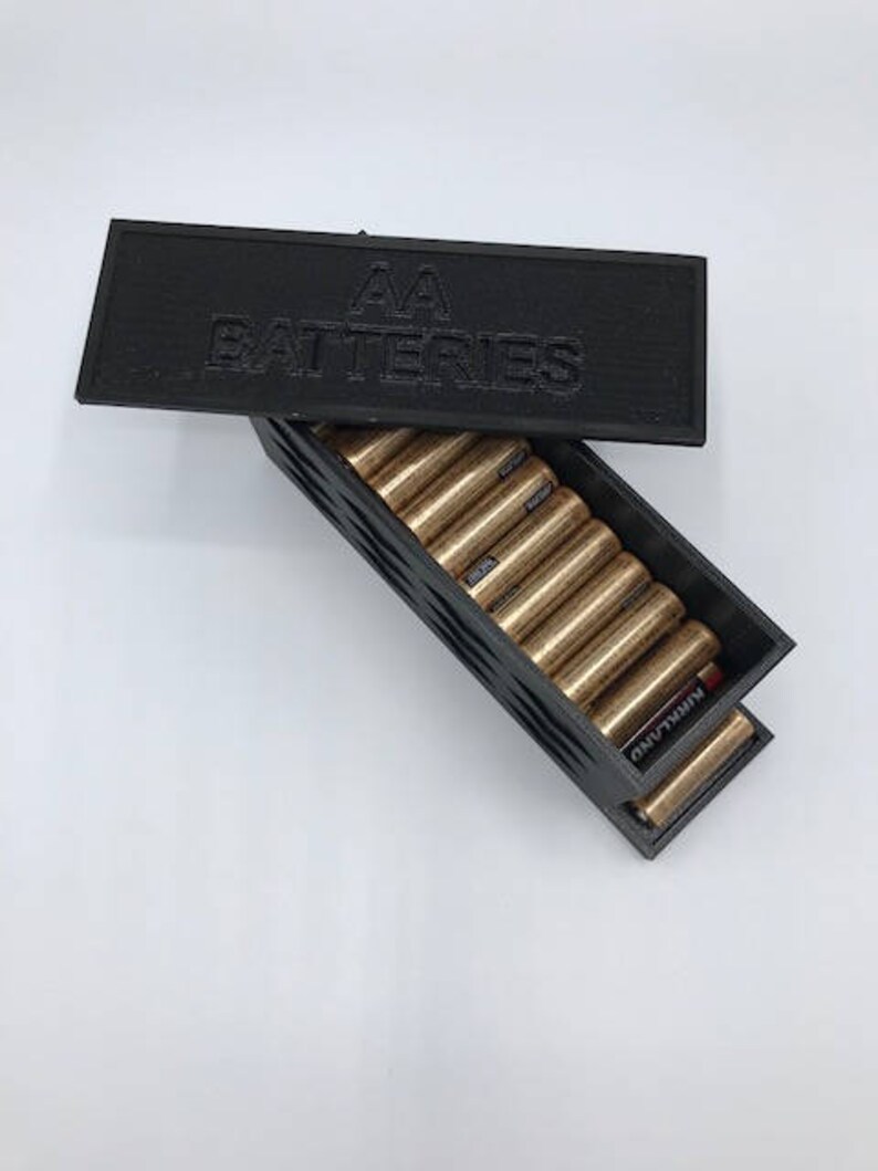 Puede incluir: Caja de almacenamiento de pl&aacute;stico negro con una tapa que dice "AA Batteries". La caja est&aacute; abierta y llena de bater&iacute;as AA.
