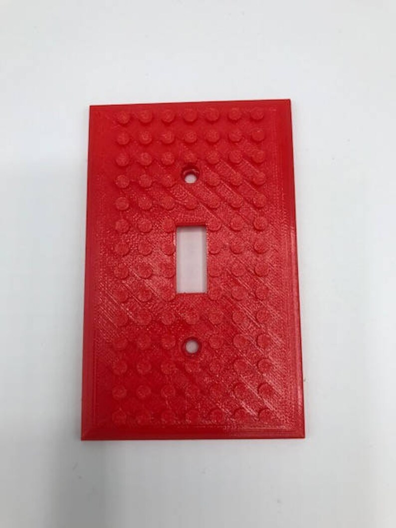 May include: A red plastic light switch cover with a textured surface that resembles Lego bricks.