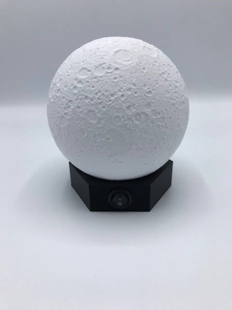 May include: A white moon-shaped lamp with a black base and an on/off switch. The lamp is designed to look like the moon with craters.