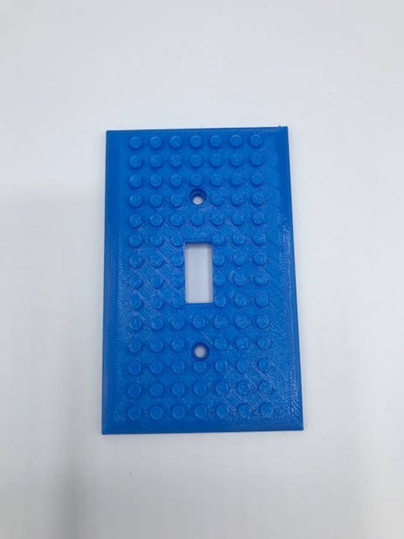 May include: A light blue plastic light switch cover with a textured surface that resembles Lego bricks.