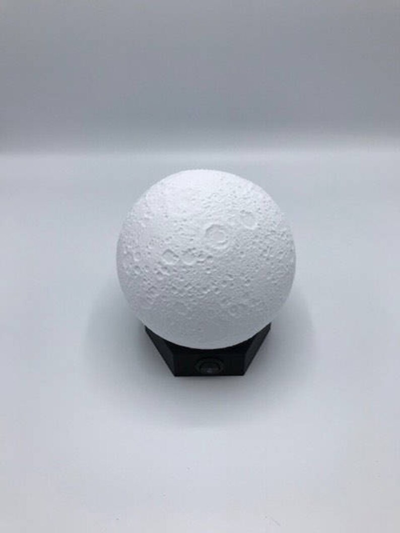 May include: A white moon-shaped night light with a textured surface, sitting on a black base.