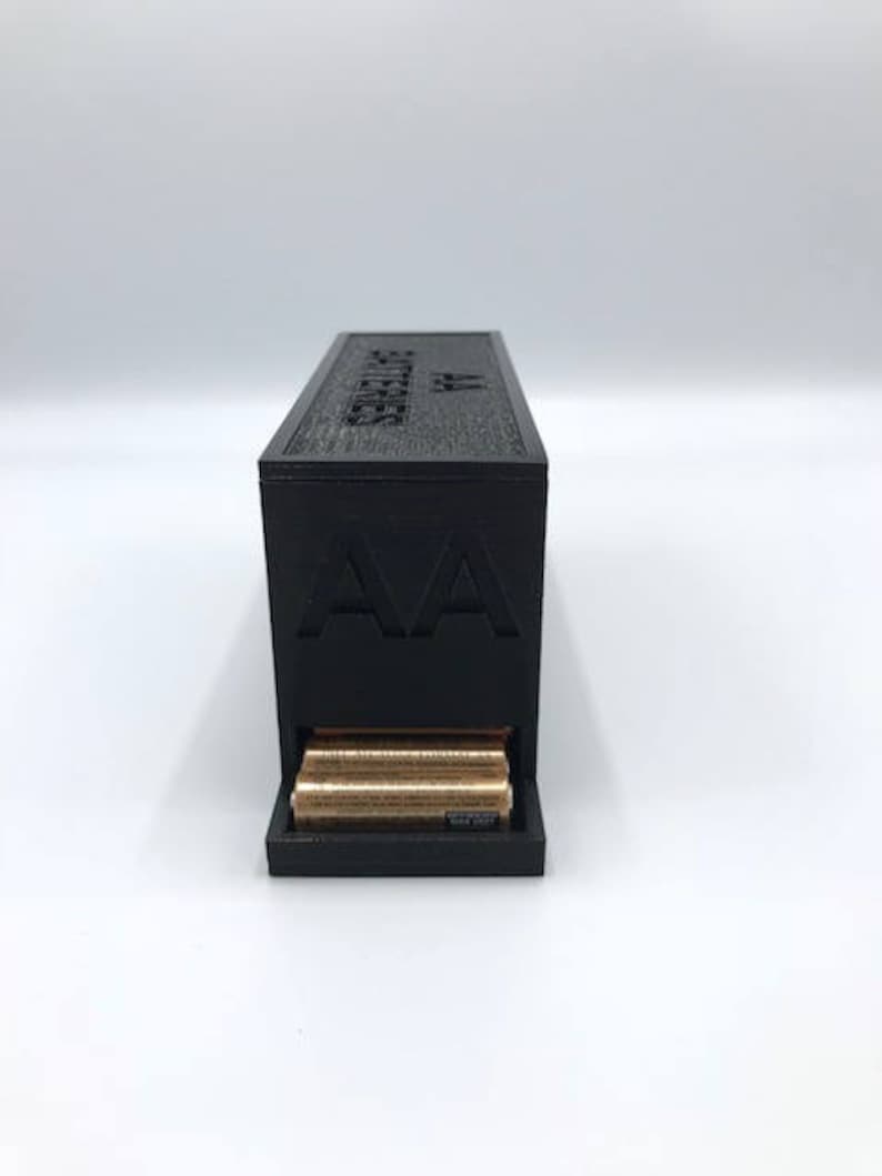 Puede incluir: Una caja de almacenamiento de bater&iacute;as negra con el texto "AA Batteries" en la parte superior y un caj&oacute;n que contiene bater&iacute;as AA.