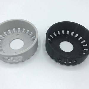 Peut inclure: Deux anneaux en plastique imprimés en 3D, l'un blanc et l'autre noir, avec une ouverture circulaire au centre et une série de fentes régulièrement espacées autour du bord extérieur.