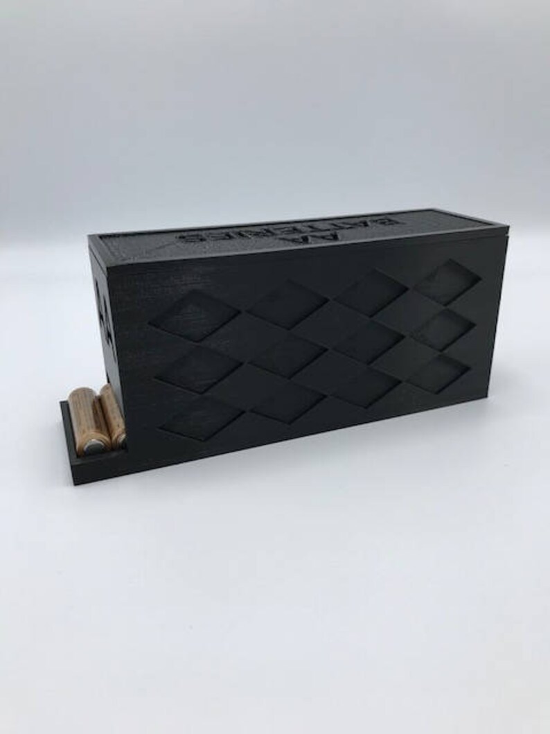 Puede incluir: Caja de almacenamiento de bater&iacute;as negra con un patr&oacute;n de diamantes y el texto "Sealed By" en la parte superior. La caja tiene un compartimento en la parte delantera para guardar bater&iacute;as.