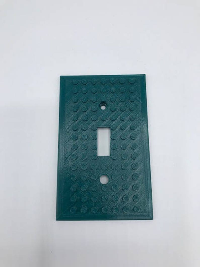 May include: A teal green light switch cover with a textured surface that resembles Lego bricks.