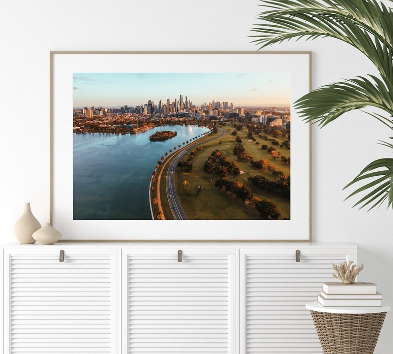 May include: An aerial photograph of a city skyline with a large body of water in the foreground. The city is in the distance and the water is surrounded by green grass and trees.