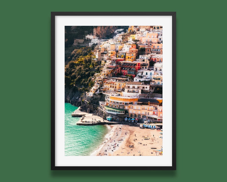 May include: A colorful, hillside town with buildings stacked on top of each other. The town is located on a cliff overlooking a sandy beach and turquoise water.