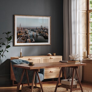 May include: A framed photograph of an aerial view of London, England, showing Tower Bridge and the River Thames. The photo is hanging on a dark grey wall above a wooden dresser and a blue armchair.
