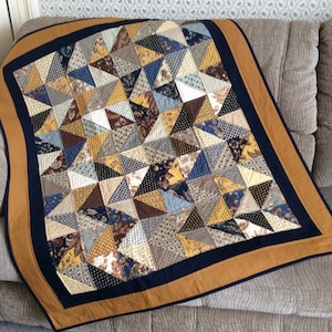 May include: A quilt with a patchwork design featuring a variety of brown, blue, and yellow fabrics. The quilt is bordered with a dark blue and a gold trim.