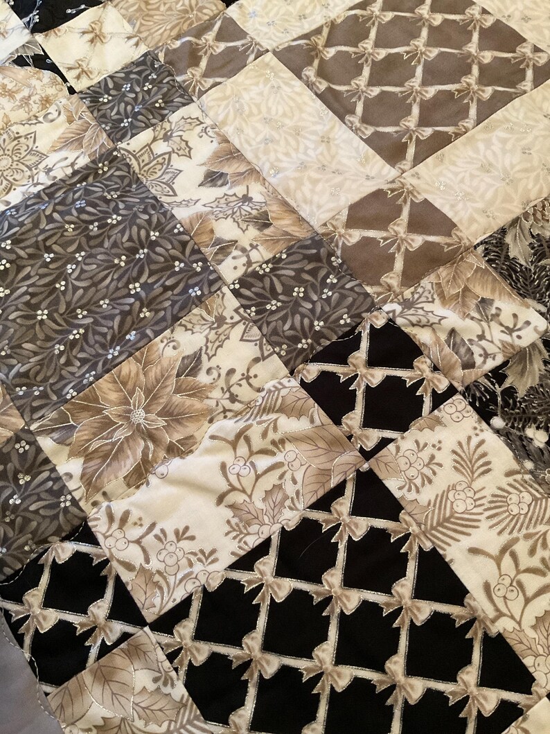 K&ouml;nnte beinhalten: Nahaufnahme eines Patchwork-Quilts mit einer Vielzahl von Mustern und Farben. Der Quilt zeigt Quadrate aus schwarzen, cremefarbenen und grauen Stoffen mit floralen, Schleifen- und geometrischen Designs. Die N&auml;hte sind sichtbar und verleihen Textur.