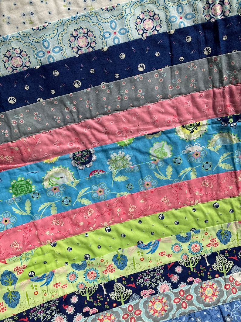 Op de afbeelding: Een kleurrijk patchwork-deken met verschillende bloemmotieven in tinten blauw, groen, roze en wit.