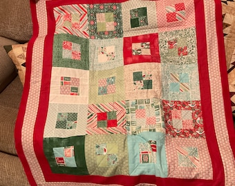 May include: A red, green, and white patchwork quilt with a red border. The quilt is made up of squares of different fabrics, each with a different pattern.