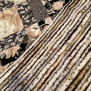 K&ouml;nnte beinhalten: Ein Patchwork-Quilt mit verschiedenen Stoffmustern. Der Quilt zeigt florale und botanische Designs in Beige, Schwarz und Grau. Ein Abschnitt hat ein Birkenrindenmuster.