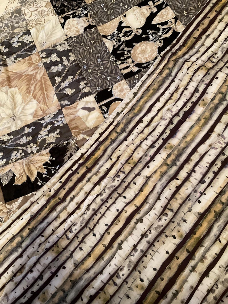 K&ouml;nnte beinhalten: Ein Patchwork-Quilt mit verschiedenen Stoffmustern. Der Quilt zeigt florale und botanische Designs in Beige, Schwarz und Grau. Ein Abschnitt hat ein Birkenrindenmuster.