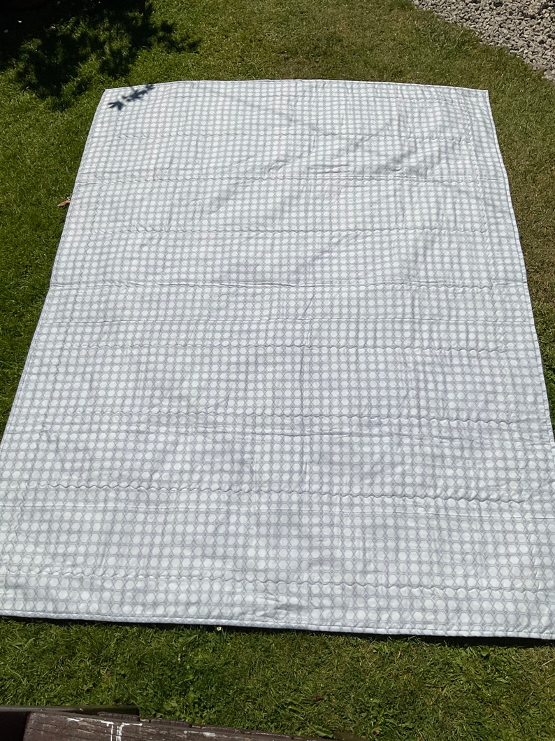 Op de afbeelding: Een wit en grijs gestreept picknickkleed met een gestikte textuur.