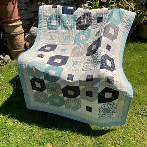 May include: A quilt with a geometric pattern in shades of blue, grey, and white. The quilt is made of various fabrics and has a light blue border.