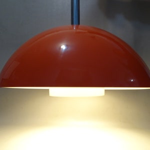 May include: A red dome-shaped pendant light fixture with a white inner shade. The light is on and casting a warm glow.