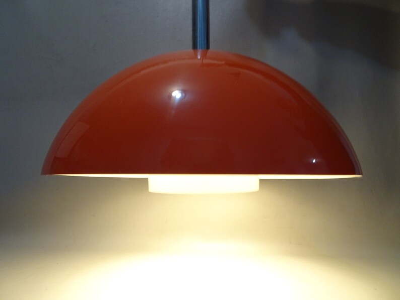 May include: A red dome-shaped pendant light fixture with a white inner shade. The light is on and casting a warm glow.