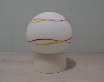 May include: A white globe lamp with red and yellow wavy lines on the surface. The lamp sits on a white base.